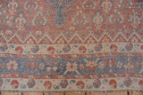 Intricate borders with faded red and blue geometric patterns showing the rug's time-softened wear.