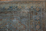 Distressed West Persian rug corner: worn pile revealing foundation, faded teal and copper patterns.