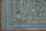 The Hamadan rug's corner with its meandering terracotta vine and dusty blue geometric borders.
