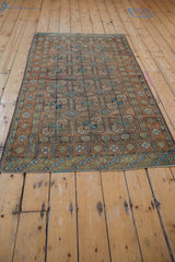 Secured end of vintage distressed Belouch rug with geometric diamond border in olive, cobalt, and chestnut.
