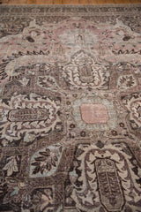 Distressed vintage Khoy rug pile, featuring faded mauve, charcoal, and ivory floral patterns.