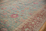 Angled view of a distressed Yezd carpet's fuchsia palmettes and contrasting burgundy border.