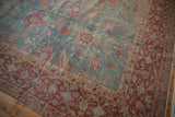 Corner of a distressed Persian rug with fuchsia palmettes on a dusty blue field and a rich burgundy border.