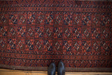 Vintage Persian Belouch rug, paneled guls in wine red, navy, and faded raspberry. Shoes on floor.