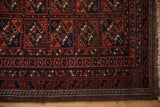 Fringed edge and geometric border of a vintage Persian Belouch rug in wine red, navy, and brown.
