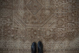 Distressed coffee brown and antique ivory Shiraz rug, geometric pattern, with visible wear underfoot.