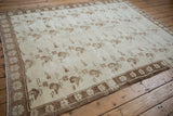 Angled view of a distressed Oushak rug's floral sprays and simple coffee brown border.