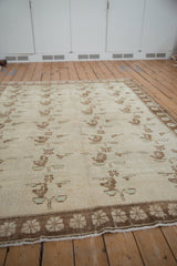 Angled view of a distressed Oushak rug showing the repeating floral spray pattern.