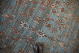 Distressed Persian Bibikabad rug with delicate vinery, palmettes, dusty blue field, showing wear, black boots.