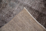 Folded vintage Overdyed Sparta carpet showing distressed brown-charcoal pile, exposed foundation, and selvage.