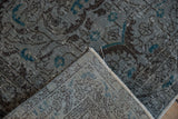 Distressed slate blue floral rug, folded to show its reverse weave and intact fringe.