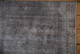 Textured corner of the distressed Sparta rug, showing oxidized silver and charcoal tones with exposed foundation.