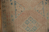 Low pile texture of a distressed Persian runner with blush and dusty blue geometric motifs.