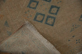 Corner view of a distressed Persian rug, showing its hand-knotted back and soft textural pile.