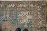 Corner of distressed Abadeh rug, intricate geometric blossoms in dusty blue and mauve tones.