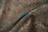 Folded detail of the distressed vintage Abadeh rug pile, featuring dusty blue and mauve floral motifs.