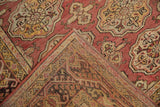 Folded corner of distressed Oushak rug, rose, gold hook and latch border, textured pile.