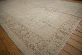 Distressed Heriz carpet corner view, showing pale ivory, seafoam, and brown geometric turtle border.
