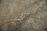 A curled edge of the distressed Tabriz rug reveals its hand-knotted weave and foundation.