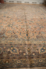 Close-up of a distressed Kashan carpet's peach field with scrolling islimis and dark aubergine border.
