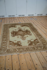 Angled view of a distressed vintage Oushak rug with an ivory field and coffee brown medallion design.