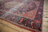 Patinated navy field, cherry red borders, and floral vinery on antique Farahan Sarouk carpet corner.