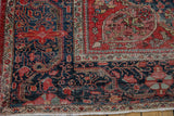 Fringed corner of an antique Farahan Sarouk rug, highlighting worn navy field and red vinery.