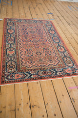 Angled perspective showing the Malayer rug's dusty rose floral field and navy blue borders.