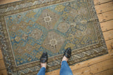 Distressed antique Caucasian rug, close-up showing worn texture, geometric guls, muted blue and sand tones.