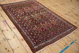 Angled view of a vintage Belouch rug showing its pomegranate garden motif and geometric borders.