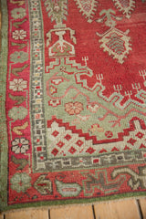 Corner of Vintage Oushak rug, cherry red and olive green geometric motifs, visible wear.
