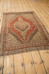 Distressed Oushak rug corner showing dusty cherry red, beige patterns, and time-softened texture.