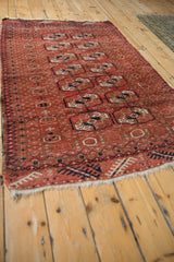 Angled view of a vintage Belouch rug's madder red field and rows of geometric Turkmen medallions.