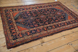 Vintage Malayer rug corner, navy field with Herati design, brick red spandrel, and worn edge.