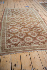 Angled view of a vintage distressed Belouch rug with a repeating geometric pattern in warm copper and ivory.