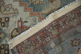 Folded Malayer rug showing worn dusty teal pile, geometric border, and woven foundation.