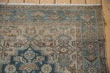 Corner detail of a distressed Persian rug showing the blue and brown floral border and ivory fringe.