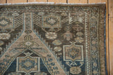 Corner detail of distressed Malayer rug, showing fringe, faded teal blossoms, and finned motifs.