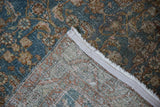Folded corner of vintage distressed Bijar rug, showing dusty blue Herati pattern, foundation, and light selvage.