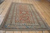 An antique Shirvan rug from an angle, showing its geometric ram's horn design and rich patina.