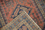 Heriz rug corner showing coral geometric pile and beige hand-knotted foundation.