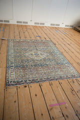 Angled view of a distressed vintage Khorassan rug showing its traditional Persian Herati pattern.