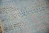Distressed pile of a vintage Khotan rug, showing faded pink pomegranates and ivory geometric borders.