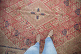 Distressed vintage Joshegan carpet, faded pink field, showing foundation and stepped medallion motifs.