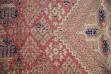 Distressed Persian Joshegan carpet close-up: dusty pink, sand, navy stylized flora and visible wear.