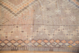 Distressed Moroccan rug close-up with geometric orange and aubergine diamond patterns.