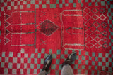 A close perspective of a vintage Moroccan rug's cherry red and turquoise geometric wool pile.