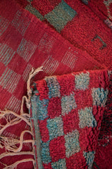 Detail of a Moroccan rug's plush checkered pile, woven back, and braided ivory fringe.
