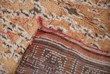 Distressed Moroccan carpet pile in faded gold and orange, exposing hand-knotted foundation with red selvage.