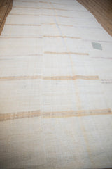 Angled view of a vintage hemp kilim runner, highlighting its storied patch and softly faded neutral stripes.